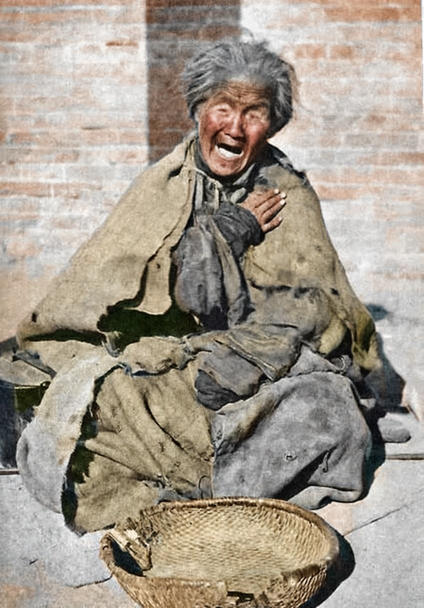 这张照片拍摄于20世纪初的北方，这位老妇人衣衫褴褛，裹着一块破旧的毯子，坐在冰冷