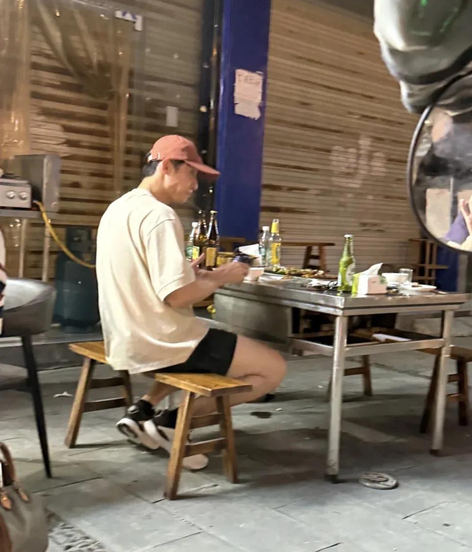 黄景瑜在乐山市一家路边摊吃烧烤，穿衣打扮很帅气，桌上放着好几瓶啤酒，路上人来人往