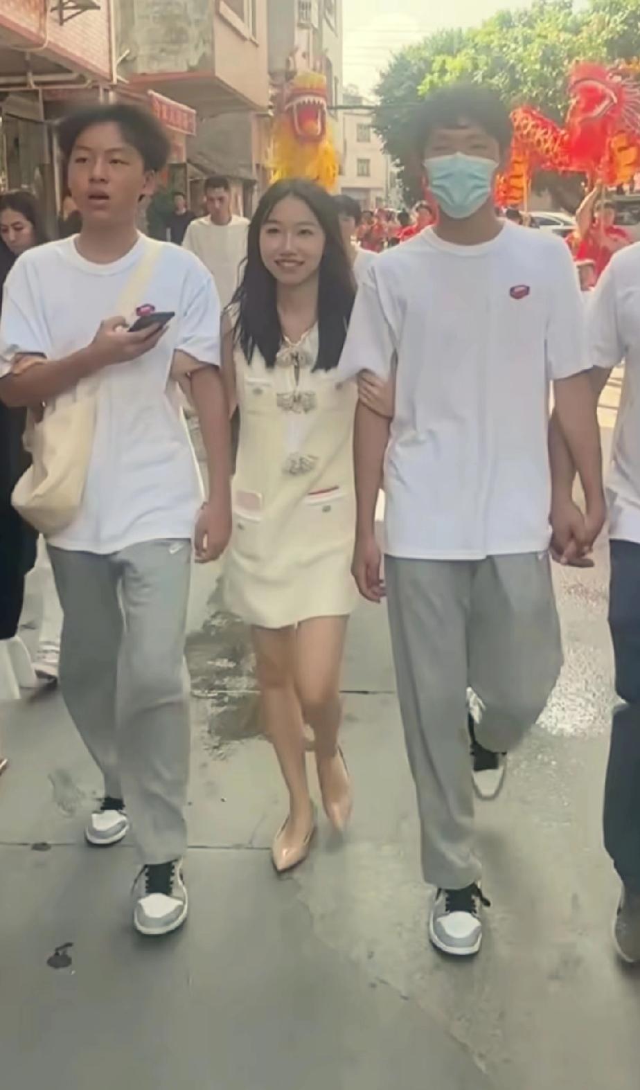 叶锐聪的姐姐与两个弟弟一同惬意地漫步街头。姐姐走在中间，双手分别搀扶着弟弟，此刻