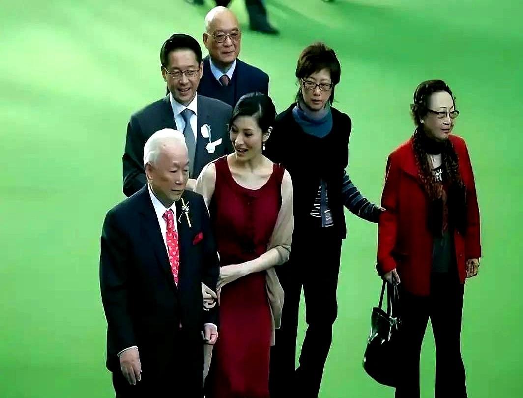 李嘉欣这边对着镜头笑得卖力，可老爷子那边完全是另一番景象。她亲手搀着90岁的