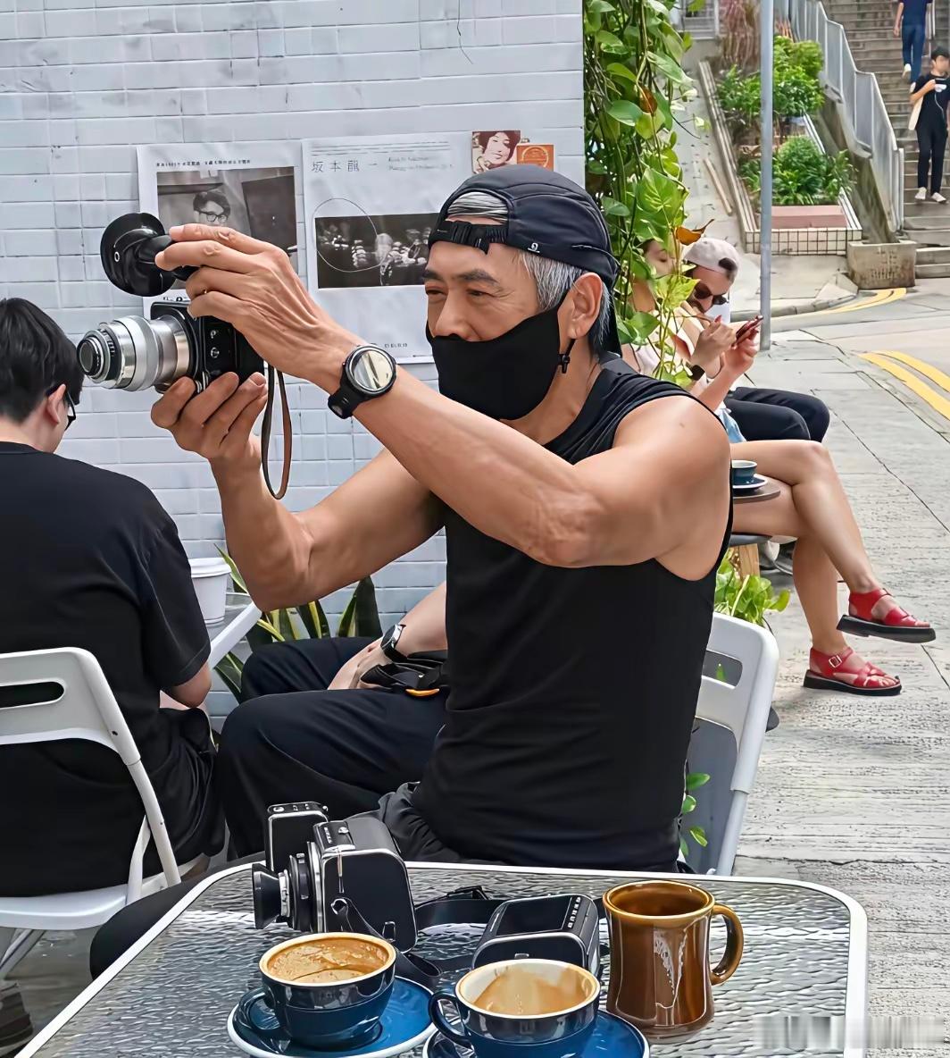 70岁周润发现身香港街头，坐在街边喝咖啡，和朋友们交流摄影技术，看起来好悠闲，他