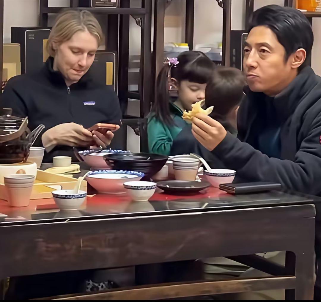 撒贝宁与外籍妻子李白以及一双儿女旅游吃早餐的一幕，撒贝宁吃着饼子，妻子吃完，看手