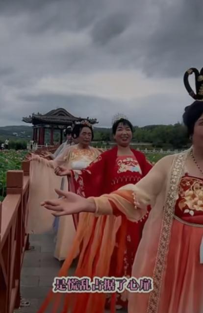 一群大妈打扮的五颜六色的大妈穿着唐装，从湖心岛的长廊迈着小碎步列队而过。网友热议