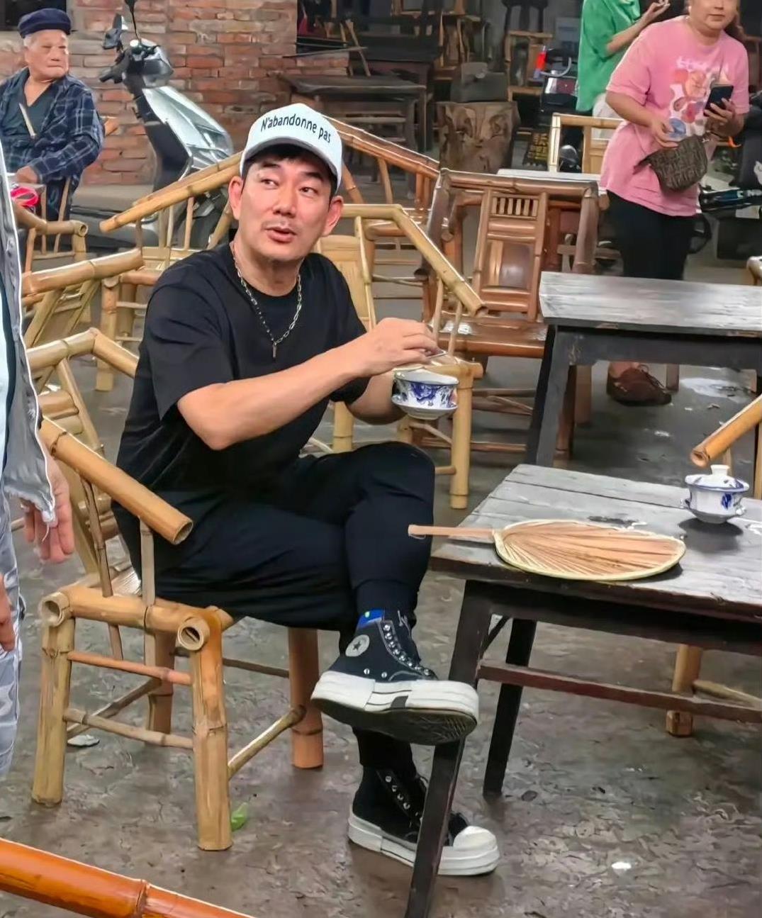 59岁任贤齐近日现身成都路边摊喝早茶，他穿着一套黑色休闲衣服，脚穿运动鞋，头顶白