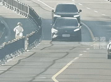 一辆轿车正常行驶在公路上，速度也不快，这时一位骑电动车的女士从另一侧穿过栅栏直挺