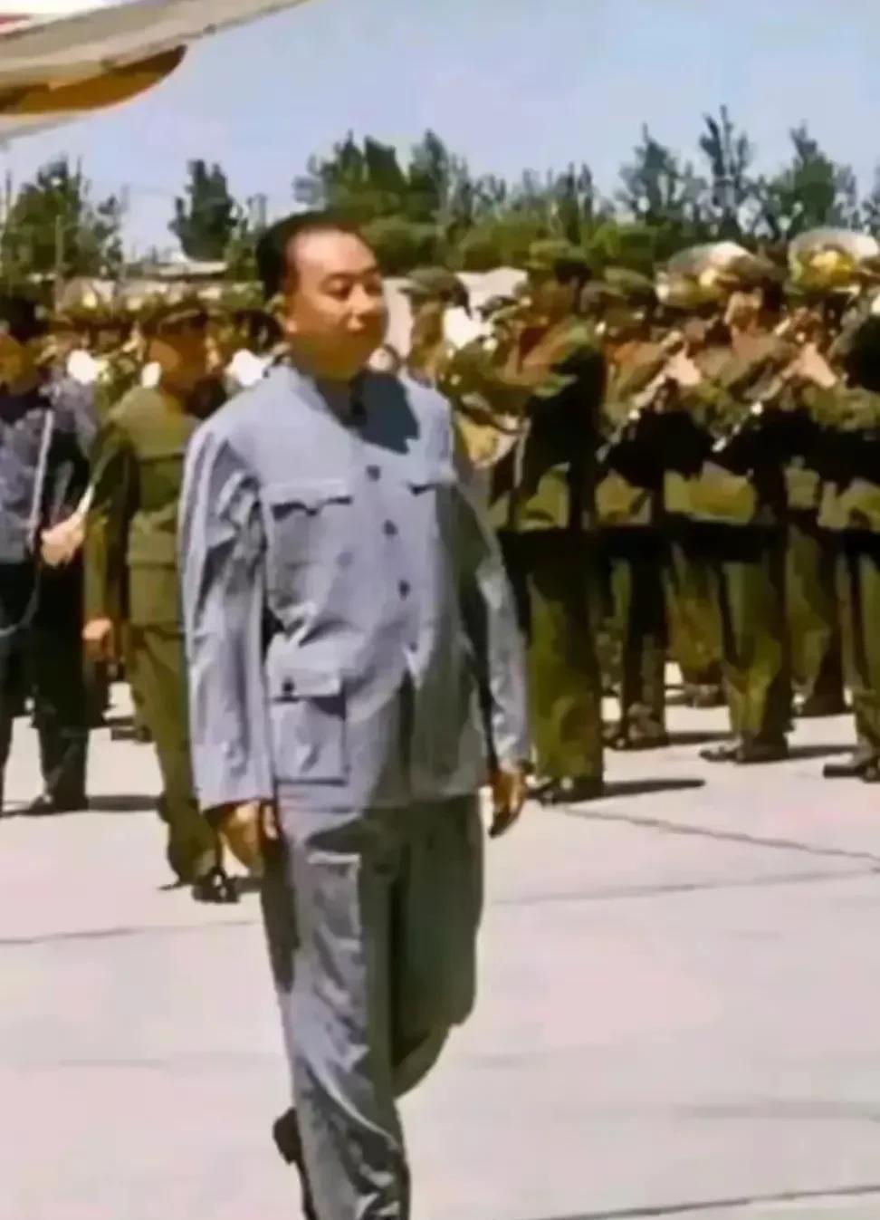 画面中华国锋正迈步在检阅部队的场地上，他身着简洁而庄重的服装，步伐坚定有力。身后