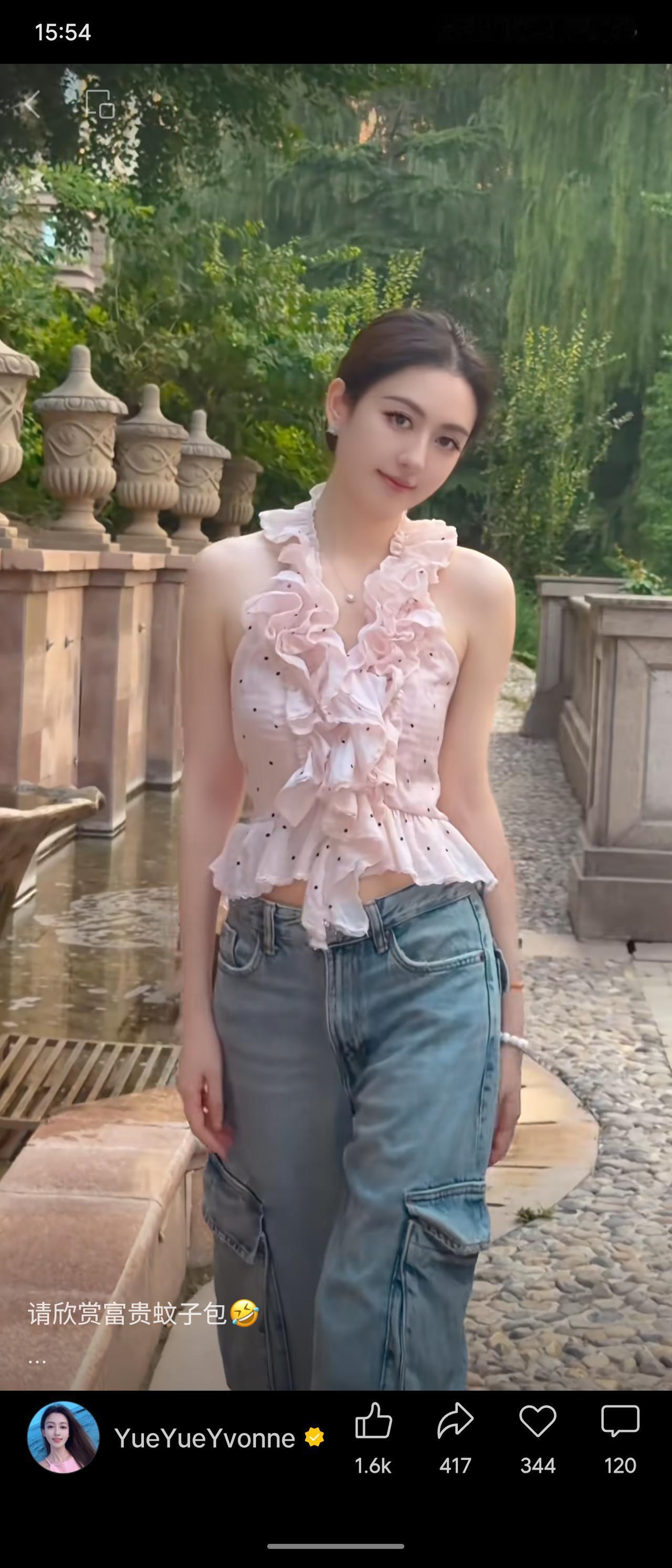 园林庭院间绿意环绕，女生梳着利落低丸子头。身着粉色波点荷叶挂脖短上衣，搭配工装阔