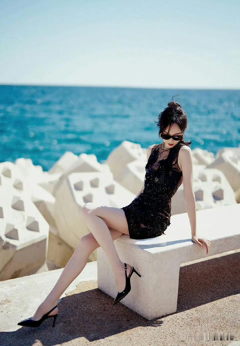 湛蓝色的海滩边,戴着黑色墨镜,身穿黑色紧身短裙搭配黑色高跟鞋的美女小姐姐,气质知