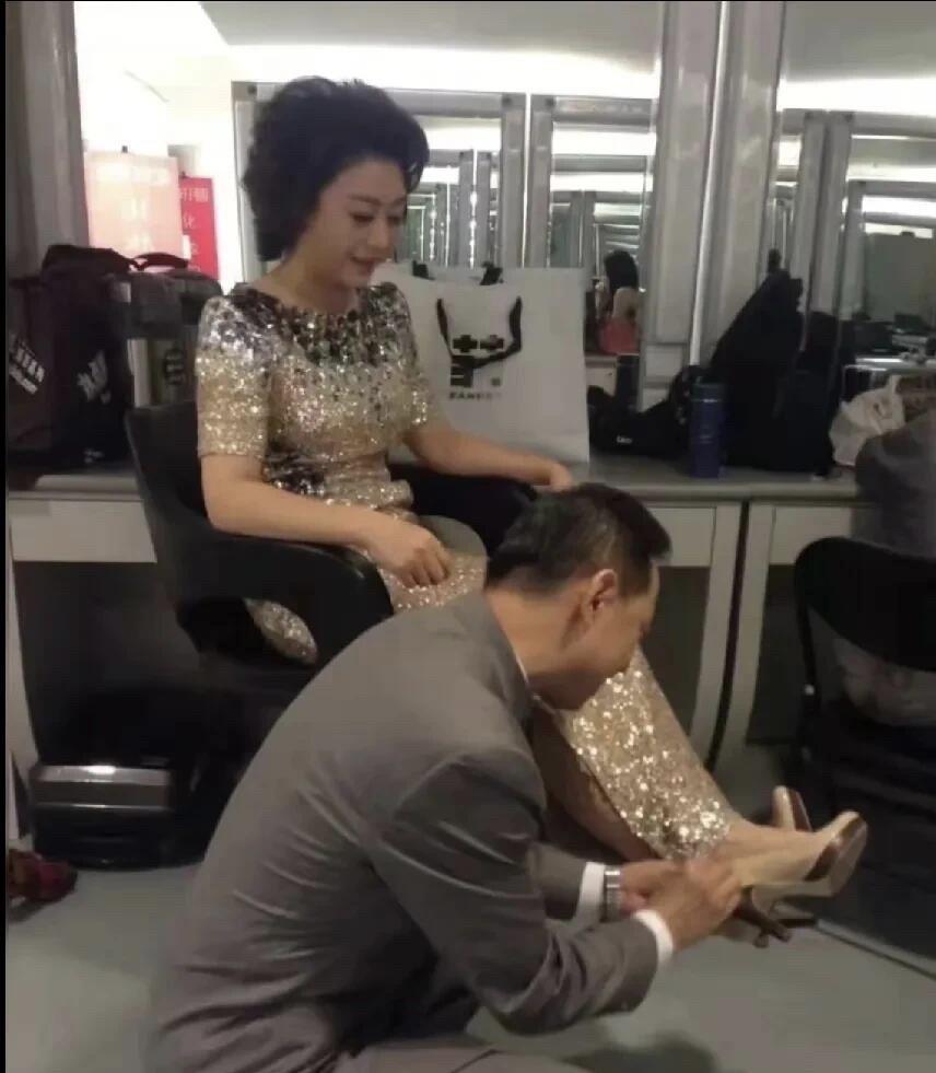 照片中穿金色礼服裙的是京剧美人李胜素，在为她穿鞋的这位男士是谁？一身西装笔挺的，
