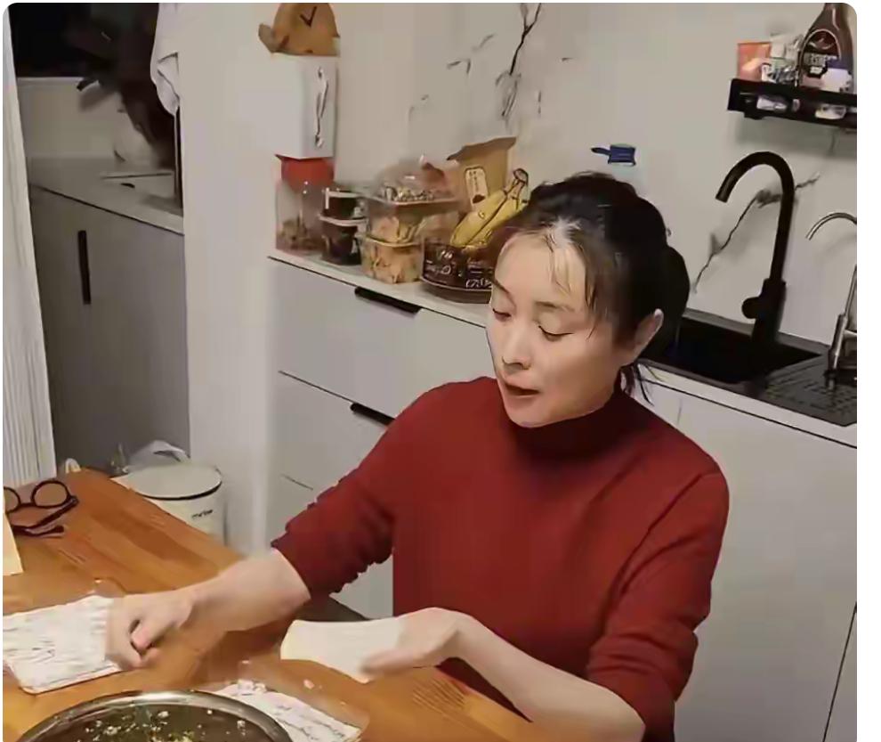 52岁的吴越独自一个人在家中包饺子，她素颜妆，穿着个红色打底衫，头发还有点凌乱，
