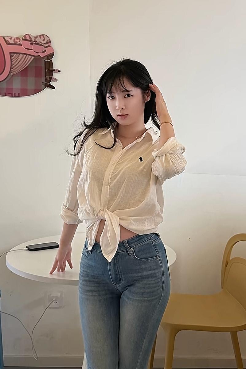 女孩站在墙边，手抚头发。