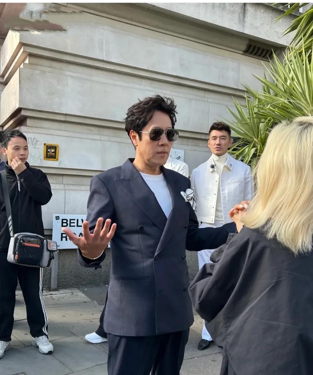 57岁的蔡国庆现身英国参加活动，戴着墨镜，穿着西装，本人很瘦，有点双下巴，嘴唇很