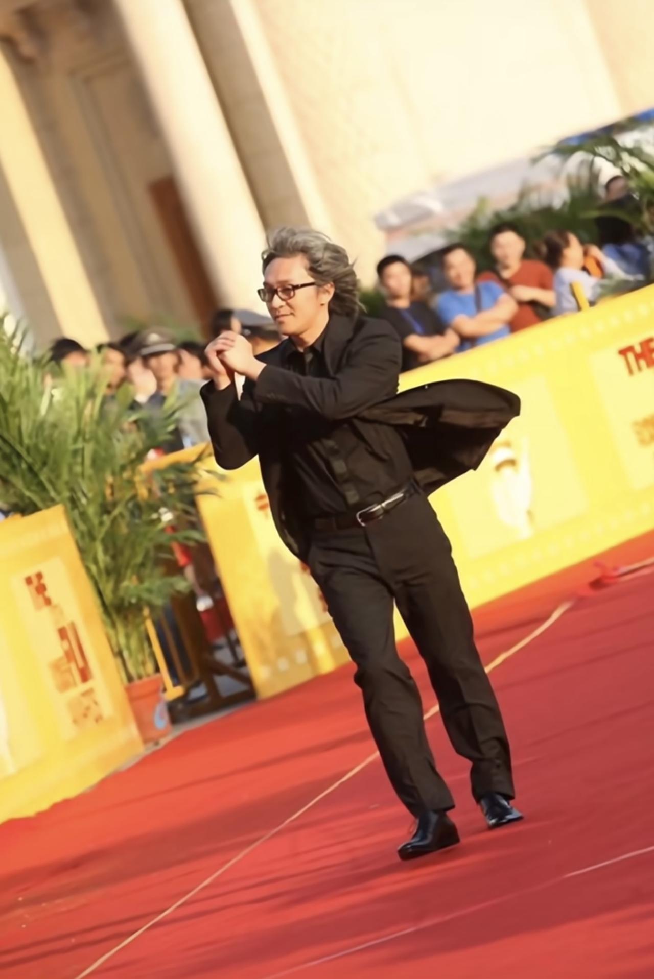 周星驰早期走红毯照，当时的风有点大，吹乱了他的头发，他在风中双手抱拳，跟大家打招