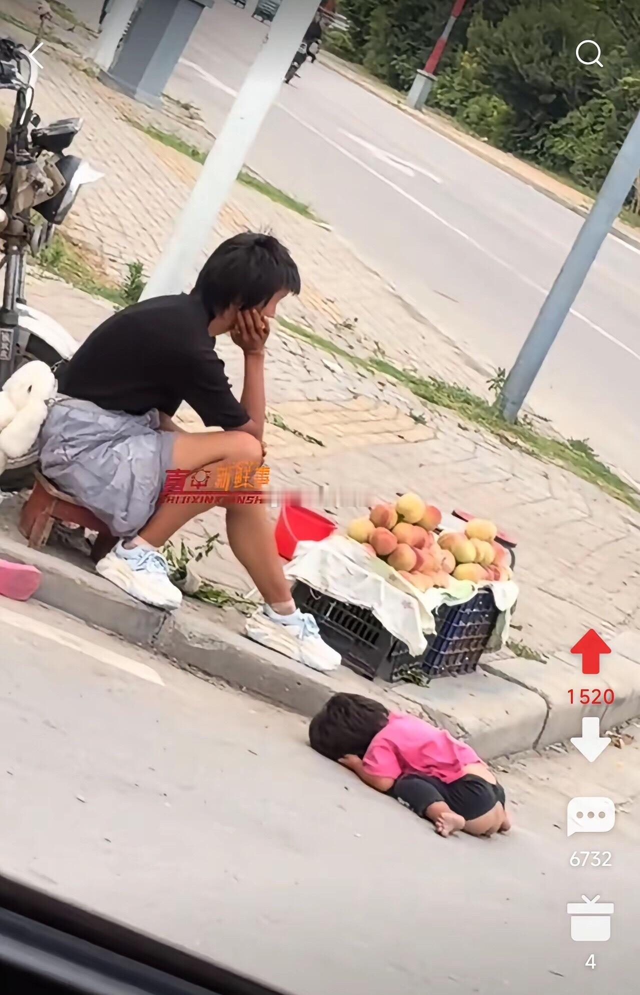 妈妈在街边卖桃子贴补家用，小女儿穿着开裆裤，趴在地上睡着了，生活不易呀！