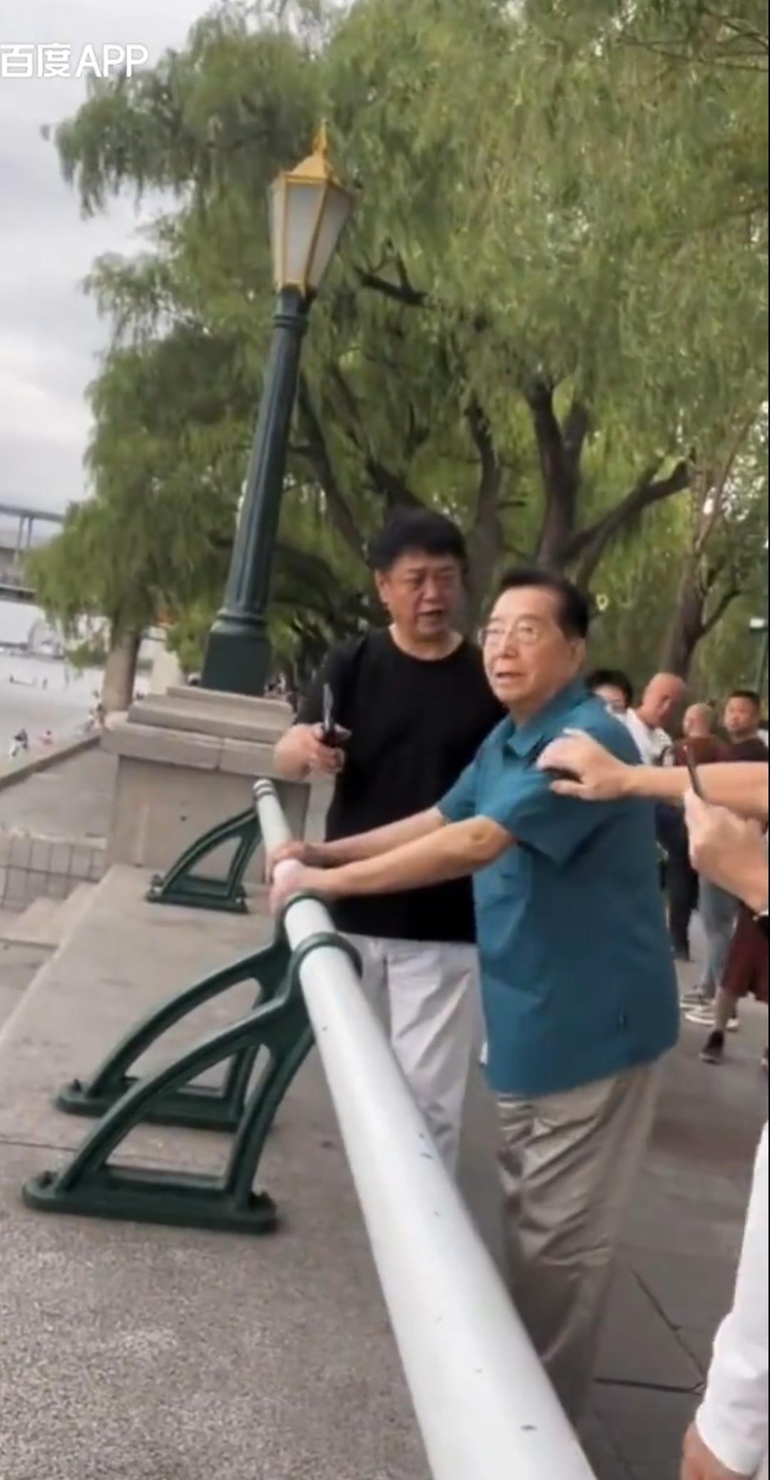 歌唱家李双江河边散步，蓝绿色短袖配白色长裤，头发乌黑，精神特好，与网友聊天特别随