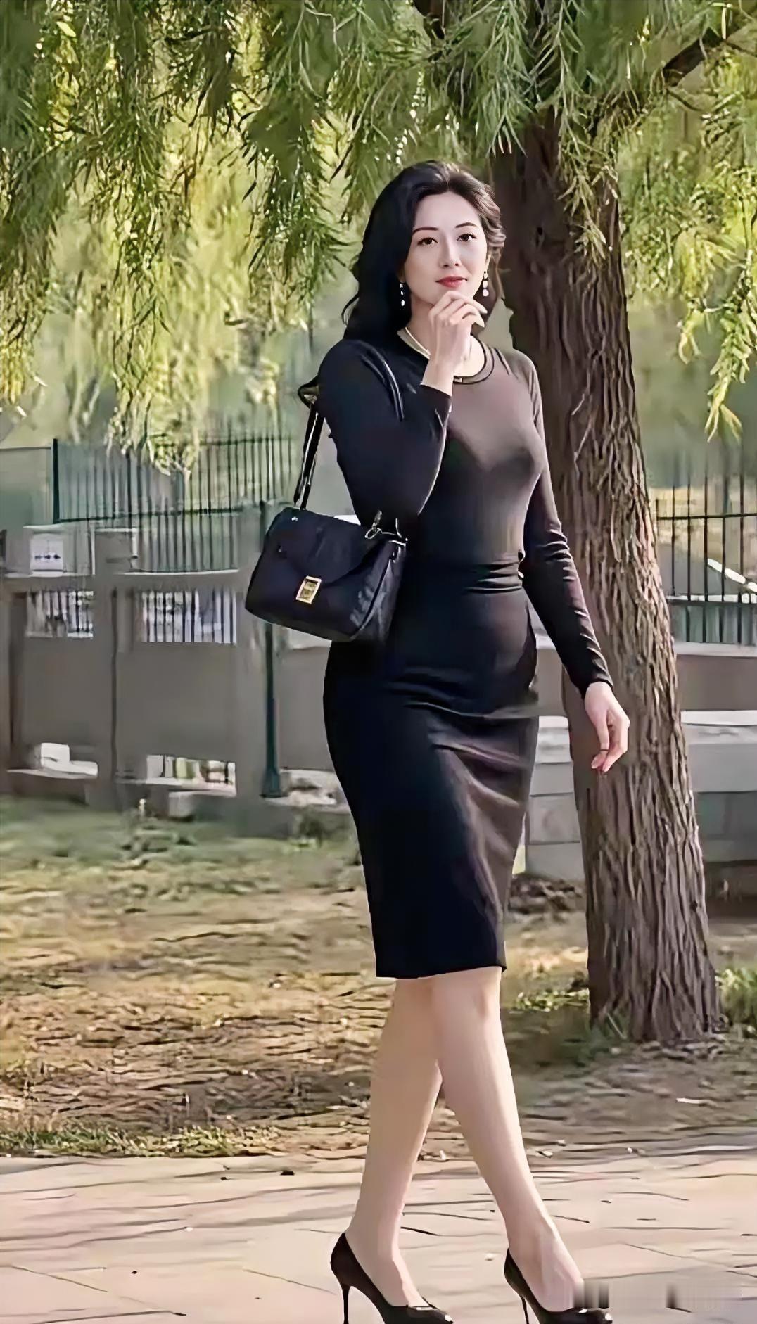 婆娑柳影下，一袭墨裙勾勒出曼妙风姿。步履轻盈间尽显从容优雅，手提包随步伐摇曳生姿