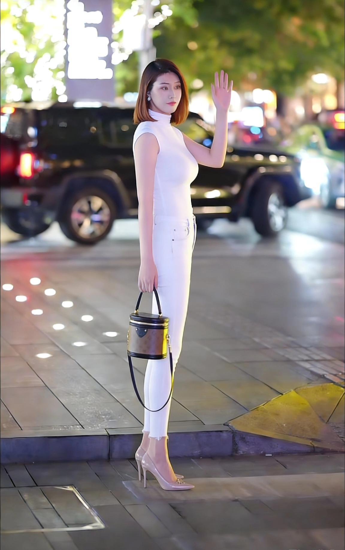 都市夜色下的优雅白衣女子，手提时尚包包，散发迷人魅力。