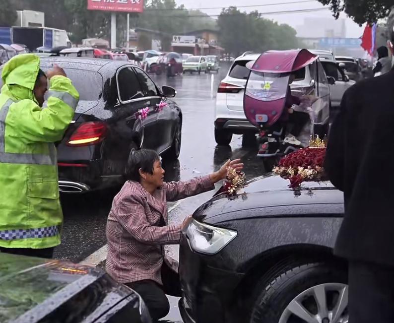 老太冒雨拦婚车，这个营业精神够狠。看车牌是河南，国庆大喜之日，却有这么些老人把不