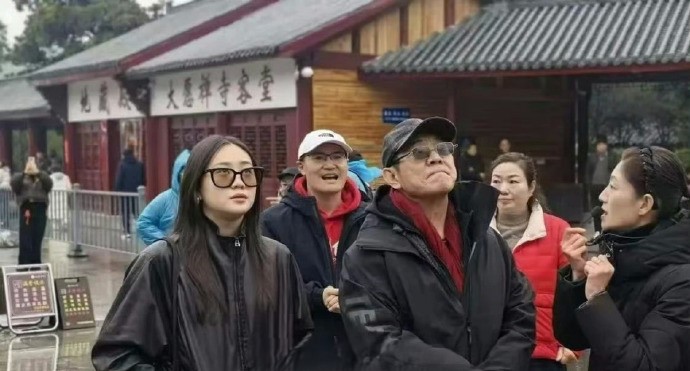 李连杰明确此行是周末家庭活动由小女儿全程陪同。父女身着黑色棉衣，在九华山阴雨天