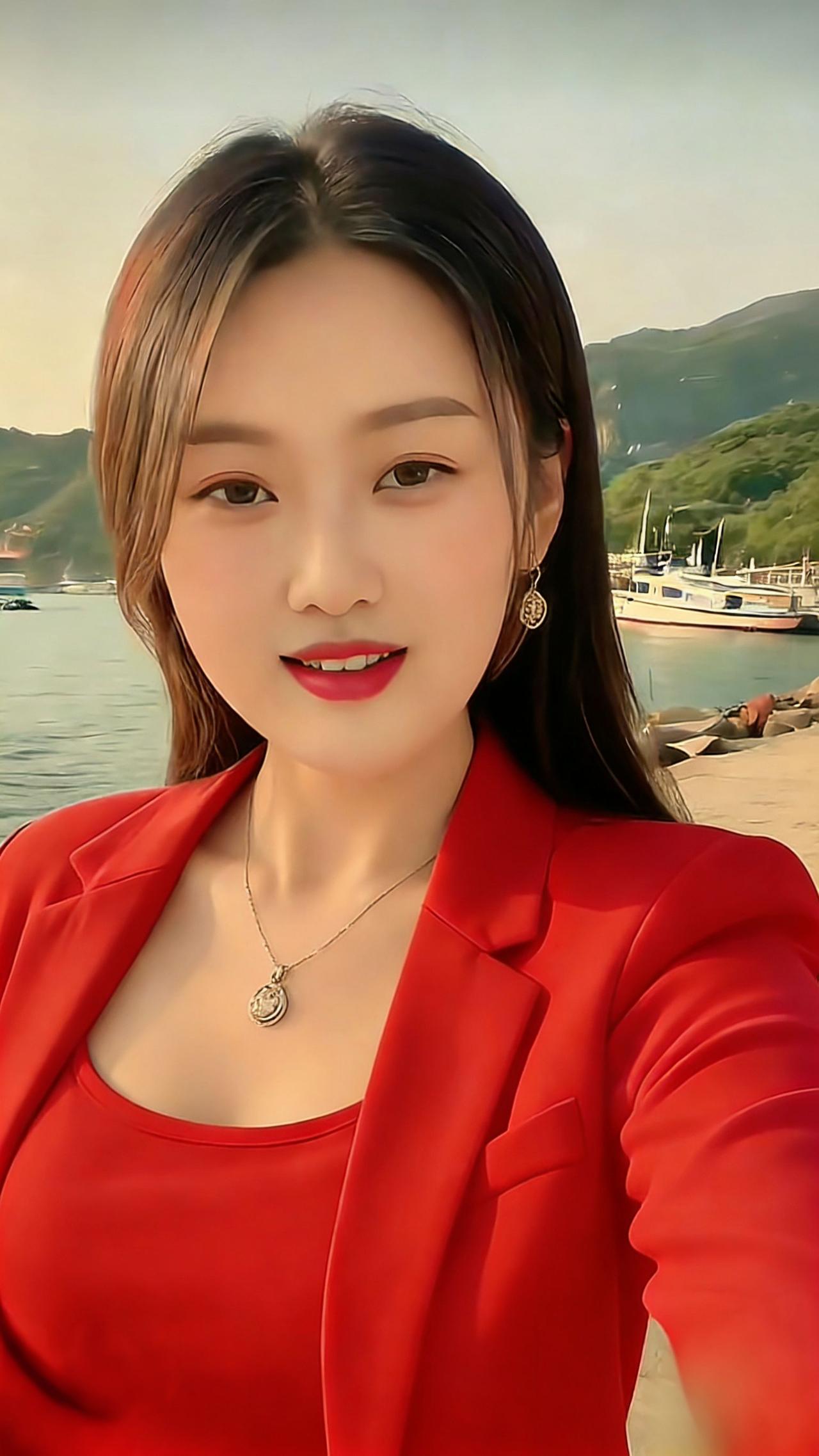 《红衫岸畔的轻暖》岸畔风裹着水汽漫开，艳红套装衬出舒展的模样，颈间坠饰轻垂