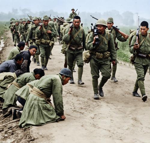 1937-1945年日军侵华期间，日军部队正沿道路行进，路边的中国平民（或被俘人