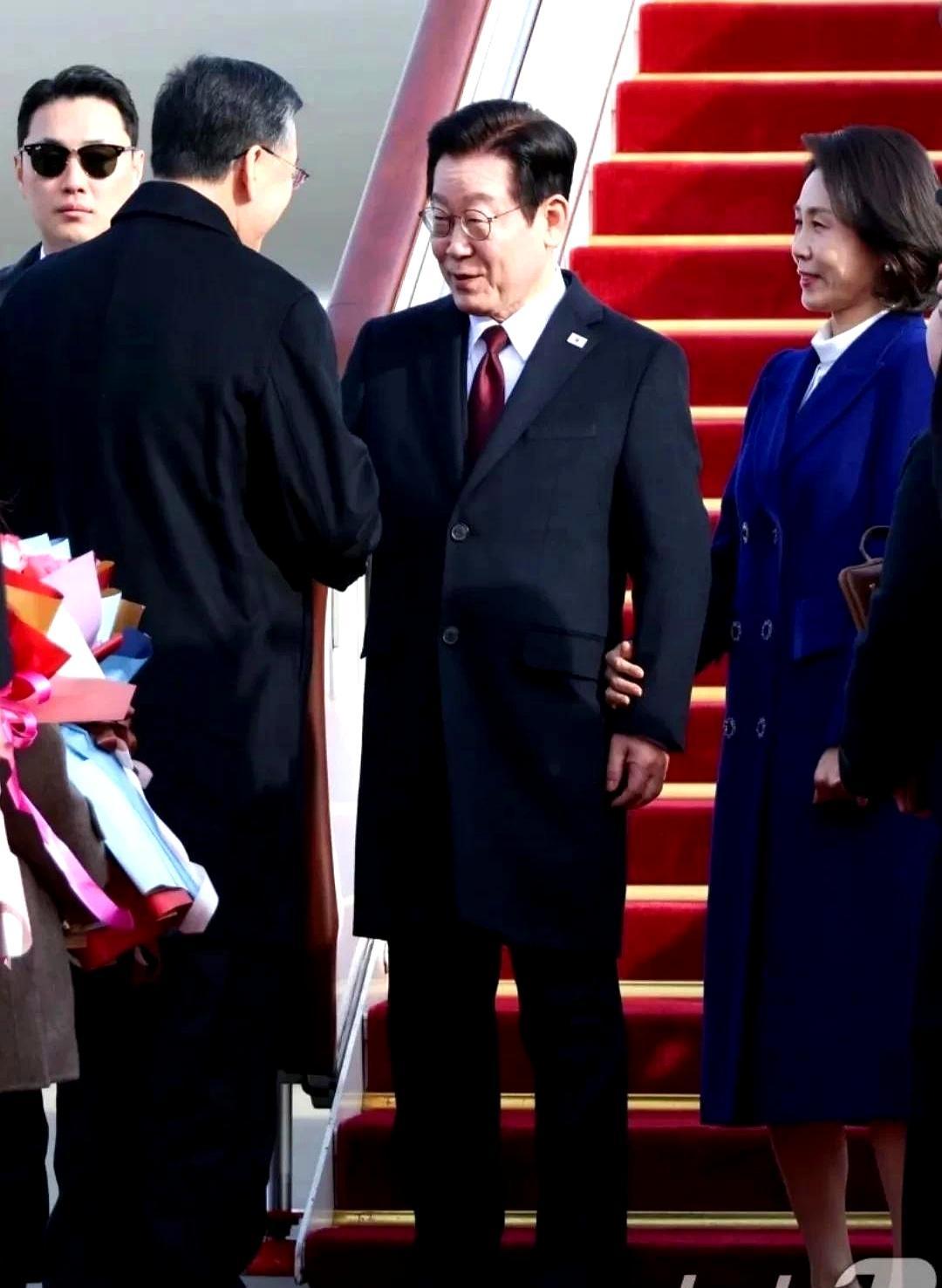 首尔机场零下三度。李在明的红领带像一道血痕划破冬日。金惠景的蓝色呢大衣下，小