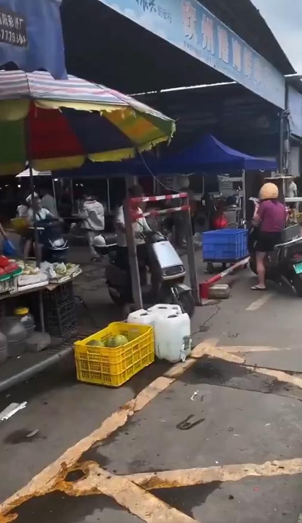 广西钦州某市场入口处低矮金属栅栏的用途是什么？视频片段显示电动车骑行者费力地弯腰
