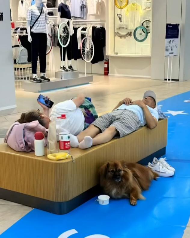 这一家三口是真会找地方避暑。大暑天里，他们直接躺在商场休息平台上吹冷气，丈夫脱鞋