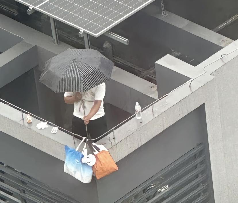 5月23日浙江一小区楼顶，一名男子背着一个小孩在天台边，男子手里拿着一把雨伞，背