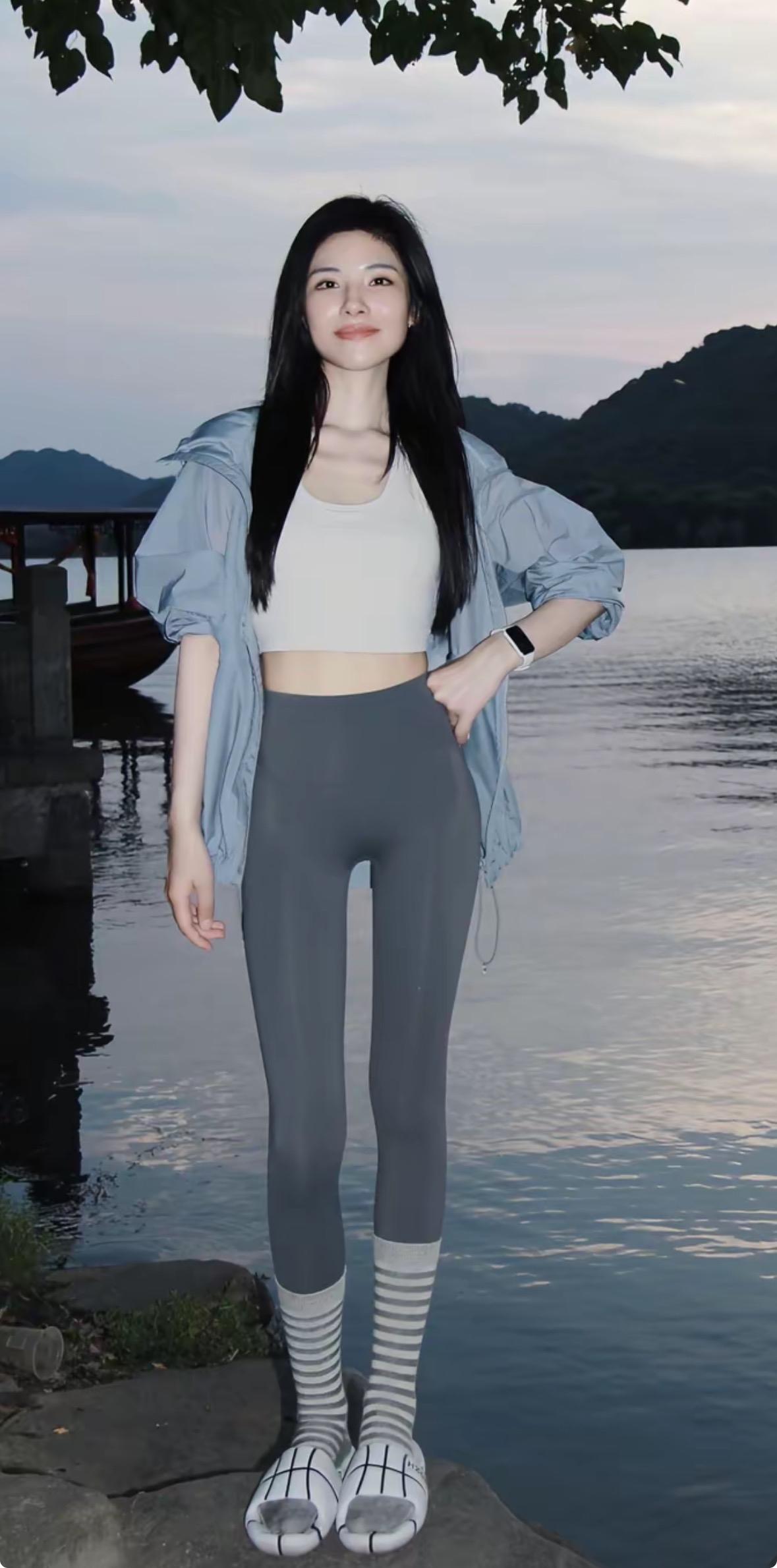 临湖而立，黑长直发随风轻扬。浅蓝防晒衣搭配白色短背心，灰色瑜伽裤勾勒修长身形，条