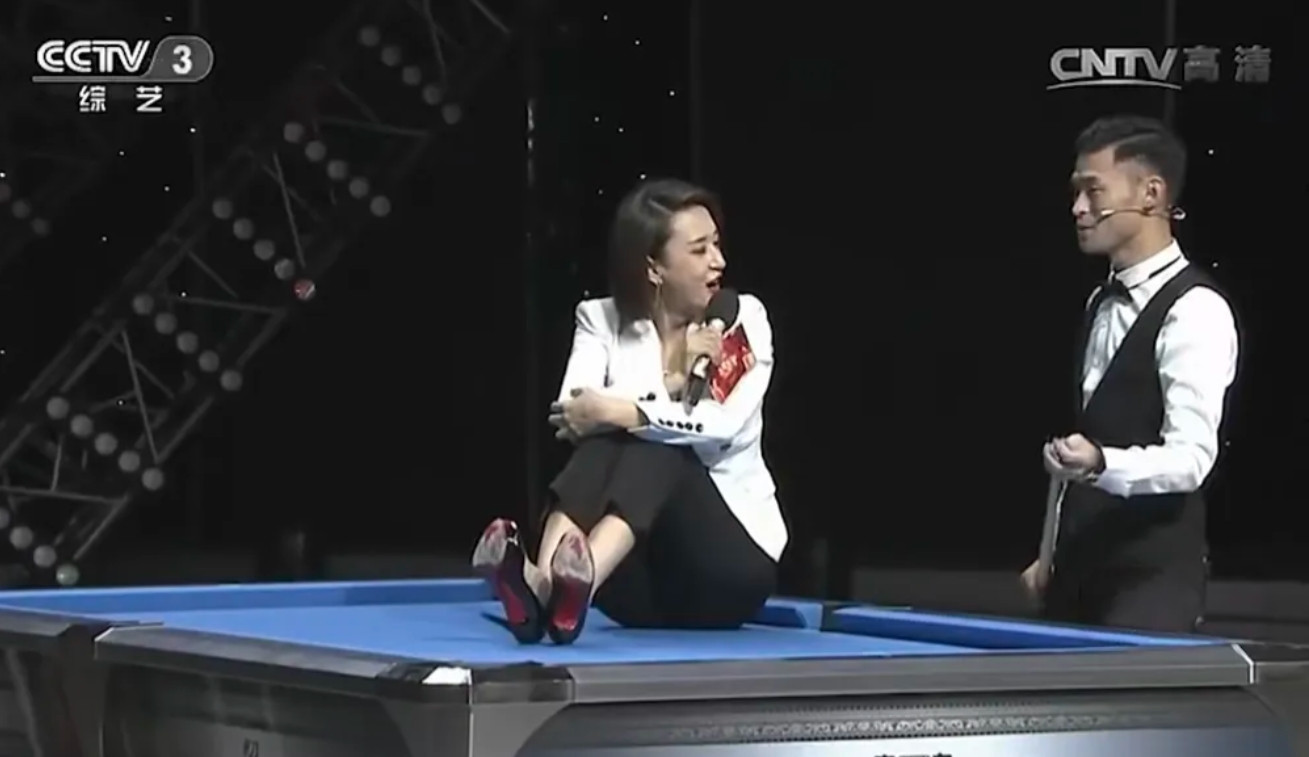美女主持人张蕾坐在台球案上，配合花式台球高手进行花式击球表演。别的不说，美女穿得