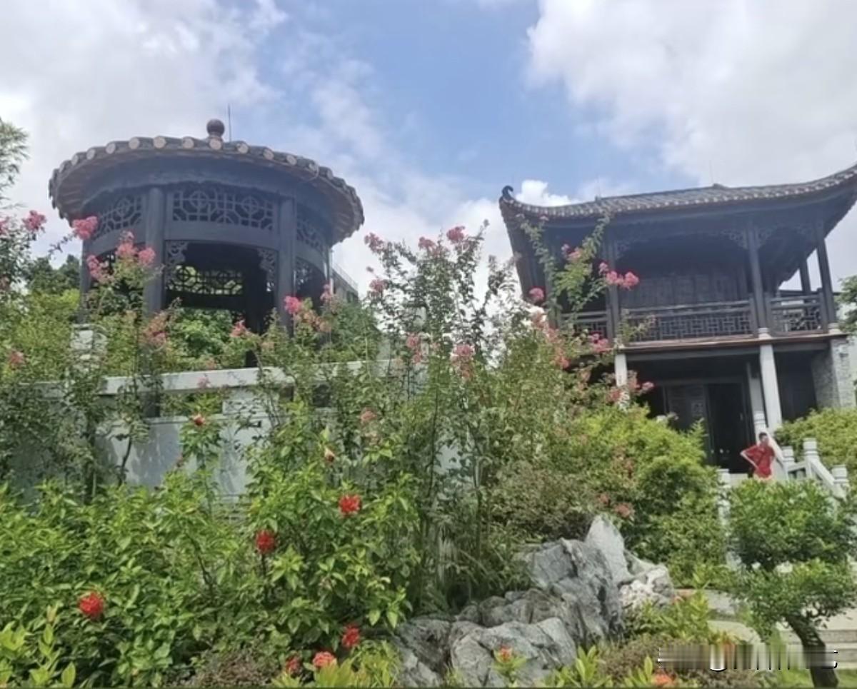 冬日生活打卡季中式亭台藏于葱茏间，黛瓦雕花与粉艳花枝相映，石阶旁怪石错落，一角红