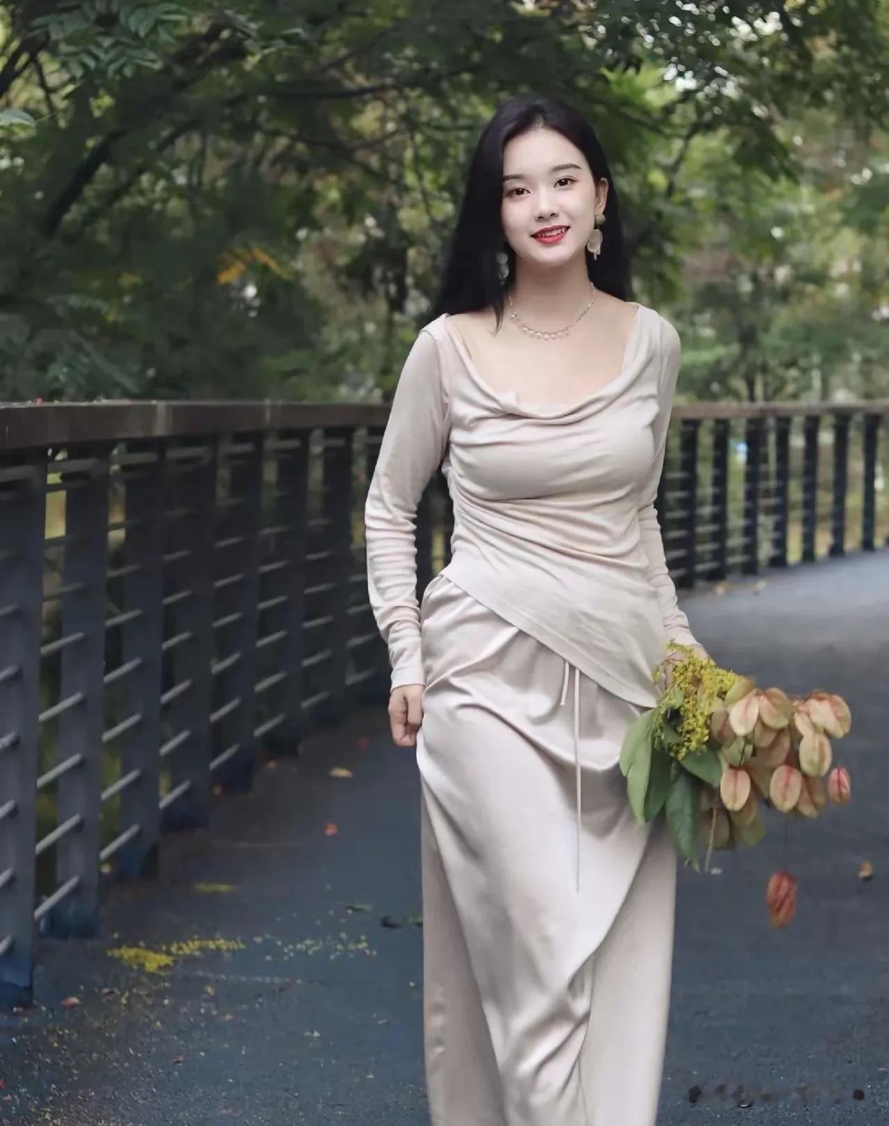她身着一袭浅米色长裙，裙摆如流水般垂坠，勾勒出曼妙身姿。领口的褶皱设计似水波轻漾