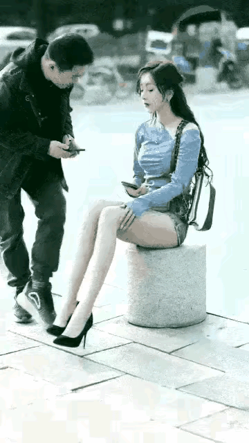 一名英俊帅气的青年男子，看中了马路边，坐在石墩上玩手机的美女。只见她肤白貌美，一