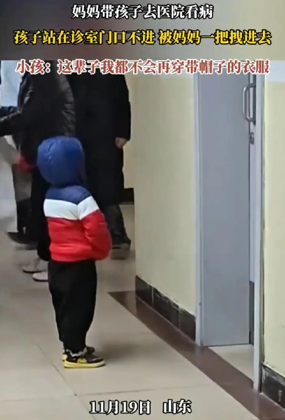 山东一妈妈带孩子去医院看病，孩子站在诊室门口不进去，被妈妈一把抓住帽子，双脚离地