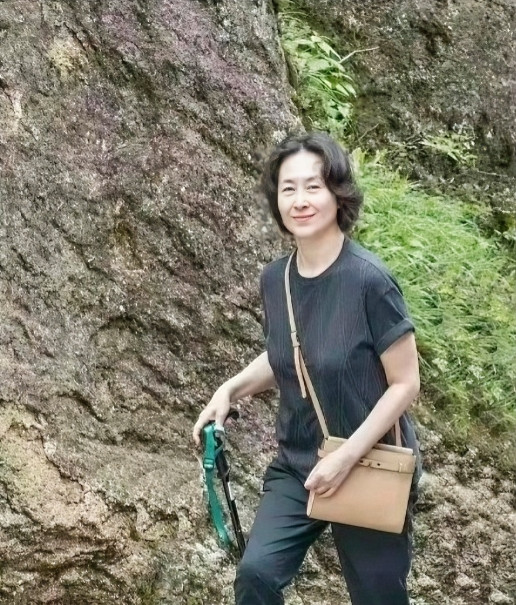 这是60多岁的何超琼在登黄山时的一个留影。图中的她穿着黑短袖黑裤轻装登山，背着浅