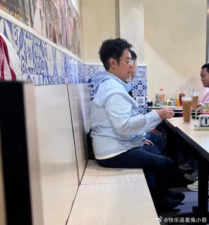 75岁谭咏麟在澳门路环码头一家餐馆吃面，他穿着足球队的衣服，留着一头羊毛卷发，身