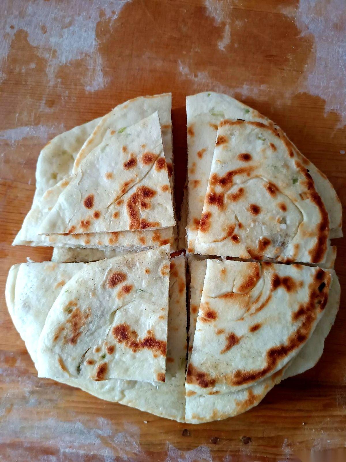 她手里的盘子一抖，差点没拿稳，刚出锅的葱油饼冒着热气，四张圆滚滚的饼摞得像小山。