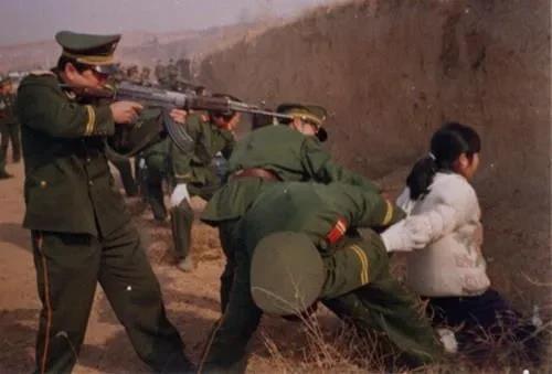 80年代，年轻的女死刑犯跪在寨墙根，一名武警举枪行刑。另外两名武警拉着女子的胳膊
