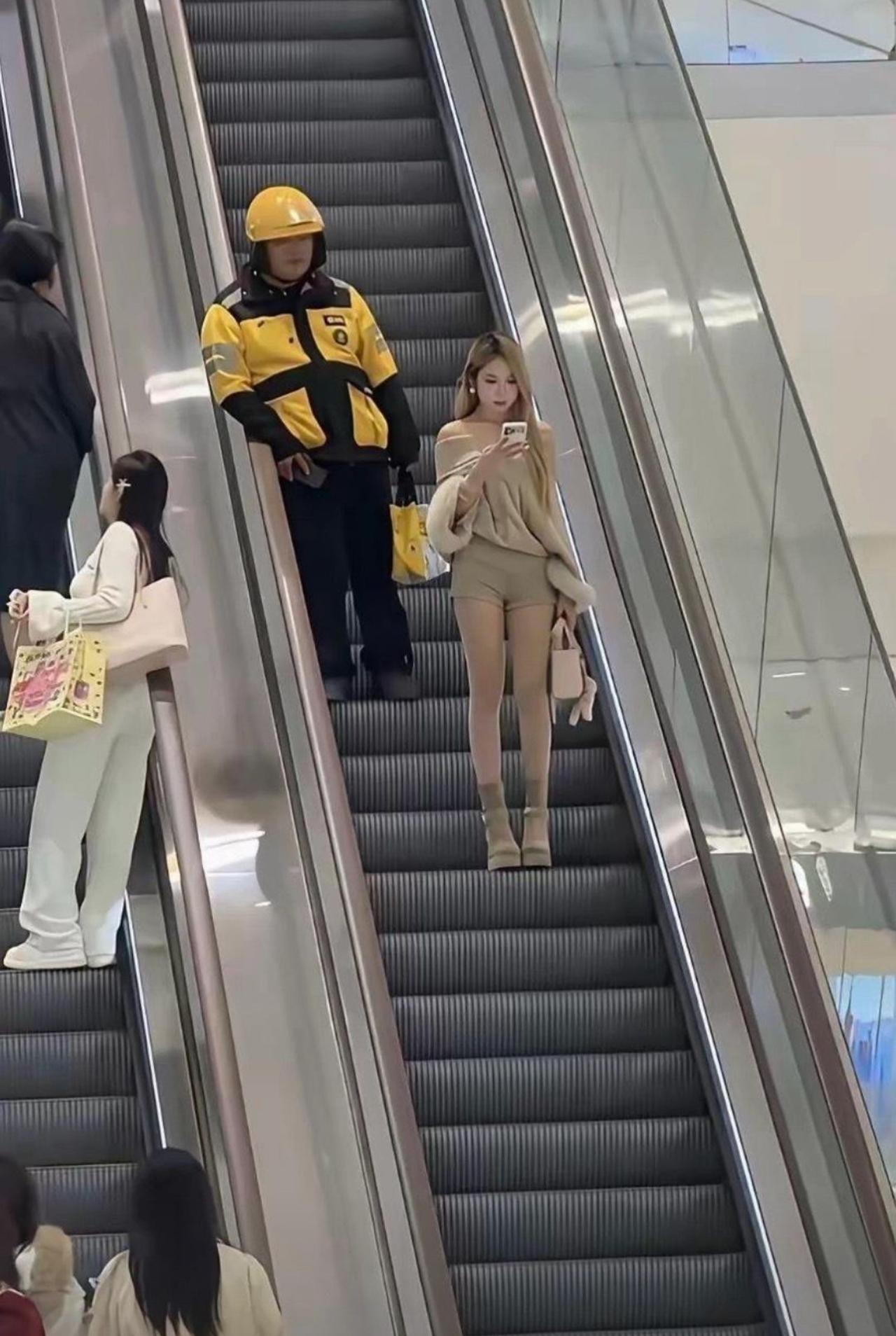 电梯缓缓往上挪，小姐姐只顾低头摆弄手机，精致穿搭氛围感拉满。身后外卖小哥直接放