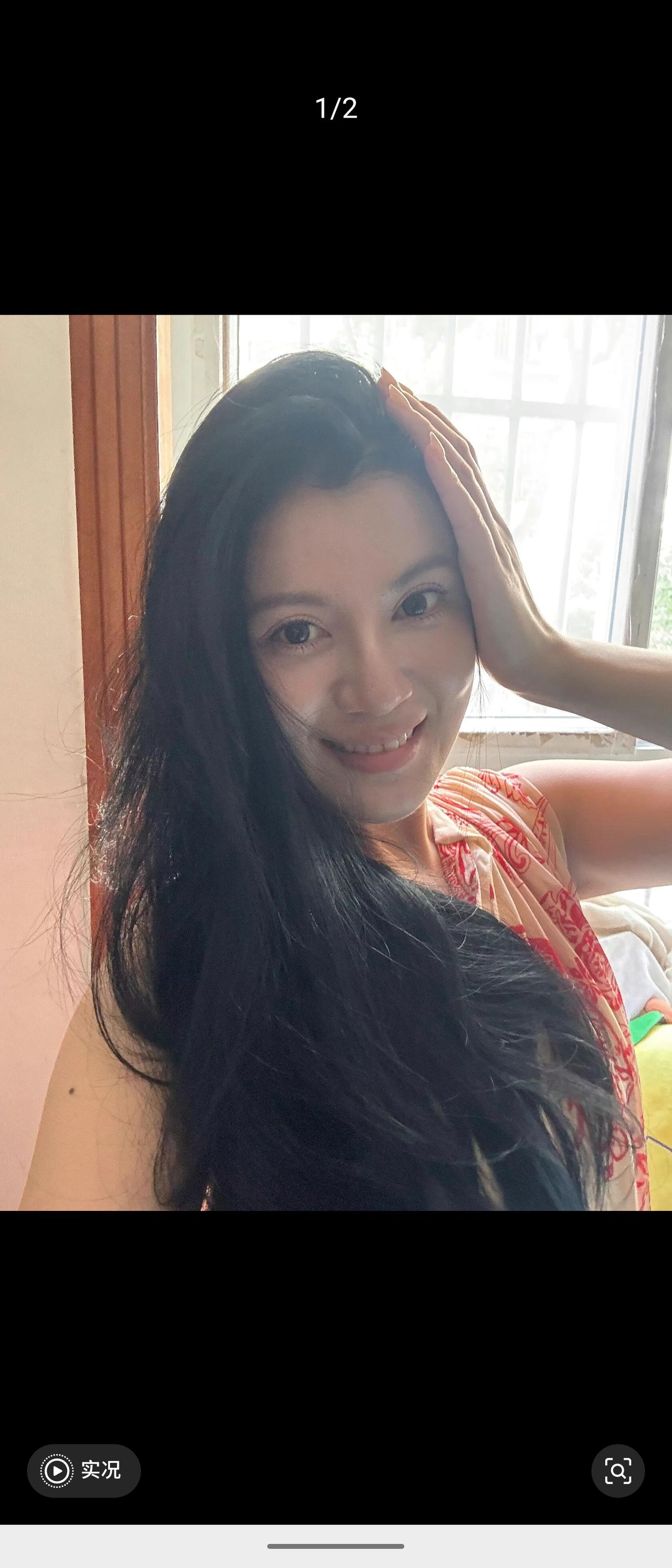 窗边暖阳洒落，乌黑蓬松的长卷发温柔垂落。她抬手轻扶头顶，眉眼明亮弯起笑意，身着浅