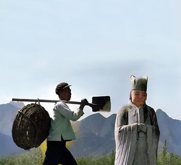 一九六四年，北京明十三陵，一名农民用铁锹背着筐子经过十三陵的石像旁。实际上，农民