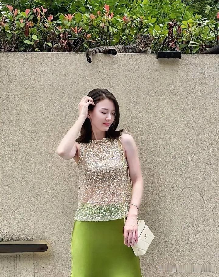 碎金亮片流转着温柔的光晕，明绿裙裾晕染夏日生机。她轻拢发丝，于素墙绿影间，宛如一