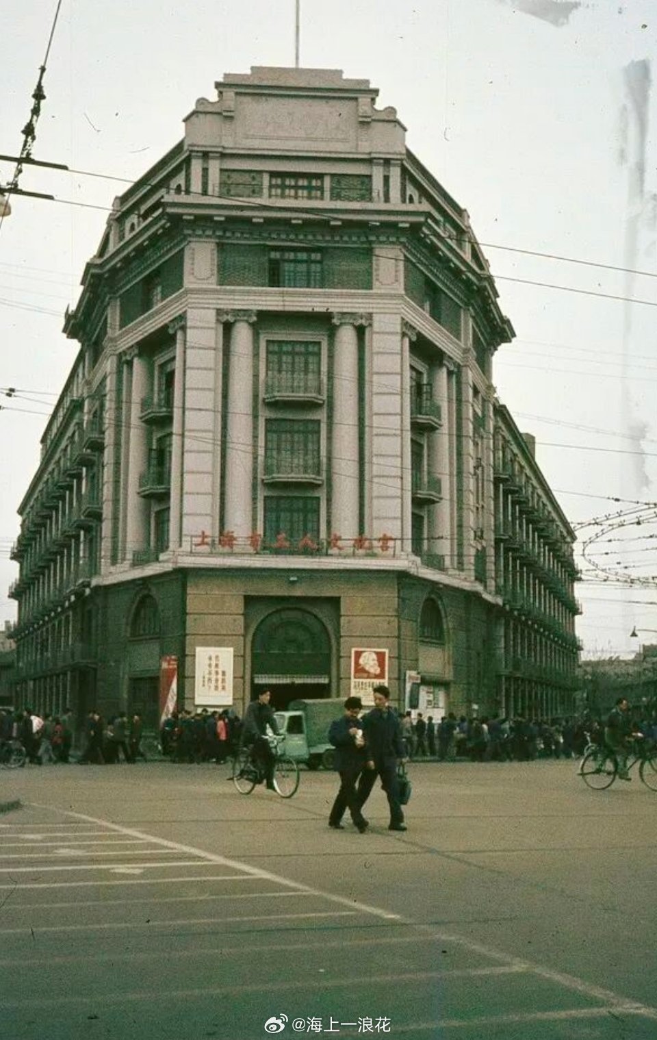 一张上世纪70年代上海市工人文化宫照片。照片中有两男子走在路中央，其中一人手拎着