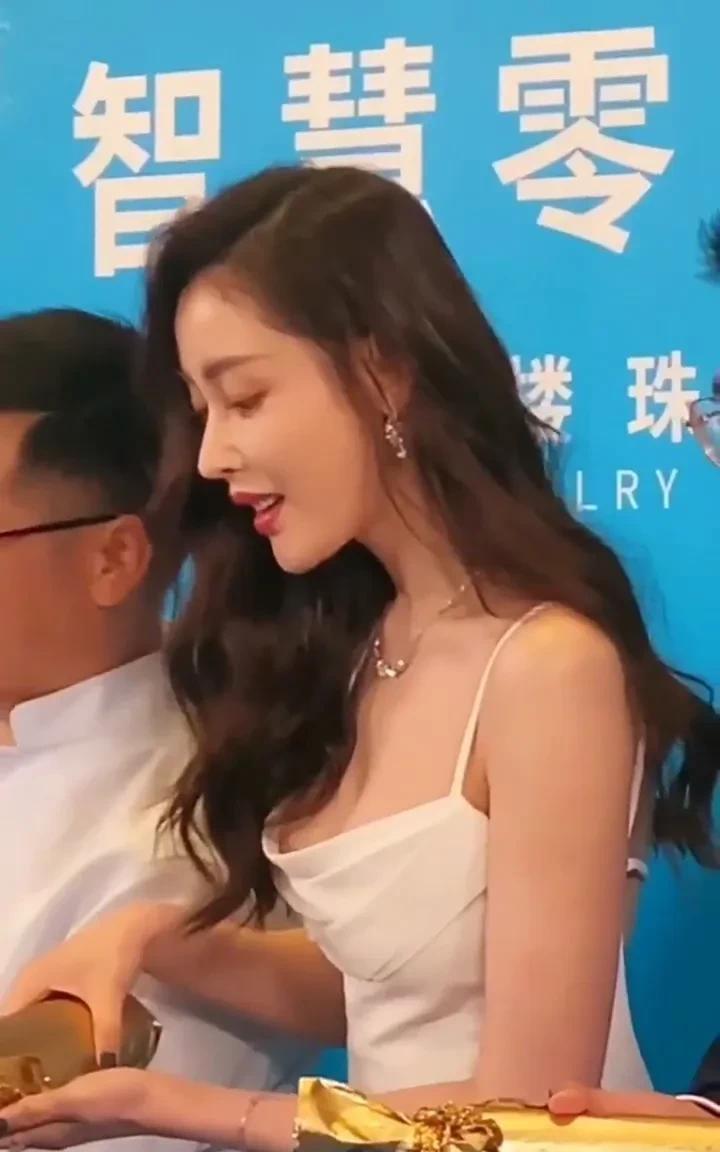 张天爱穿白吊带裙出席活动，长发微卷，红唇浅笑，手持金物，身材火辣到让活动现场灯光