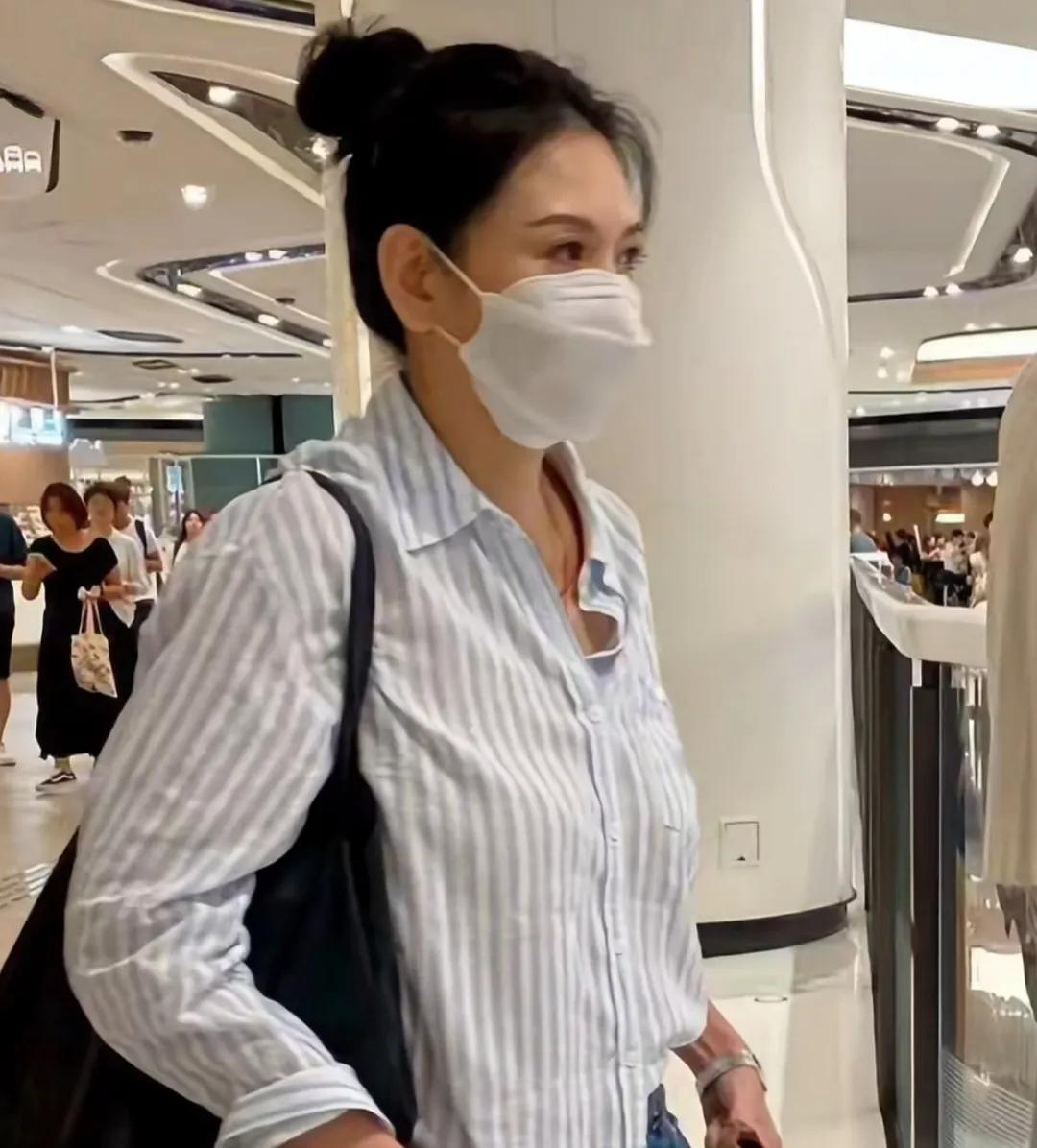 57岁邱淑贞在香港逛商场，她穿着条纹衬衫，扎着丸子头，虽然穿衣打扮低调，但身上的