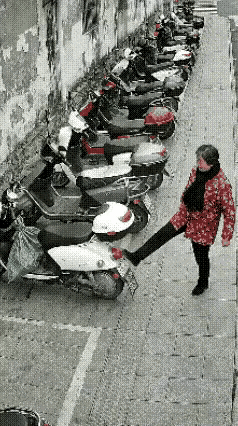 真解气！路边大妈无故踢踹别人电动车，没想到搬起石头砸自己脚，被带倒重重摔在地上，