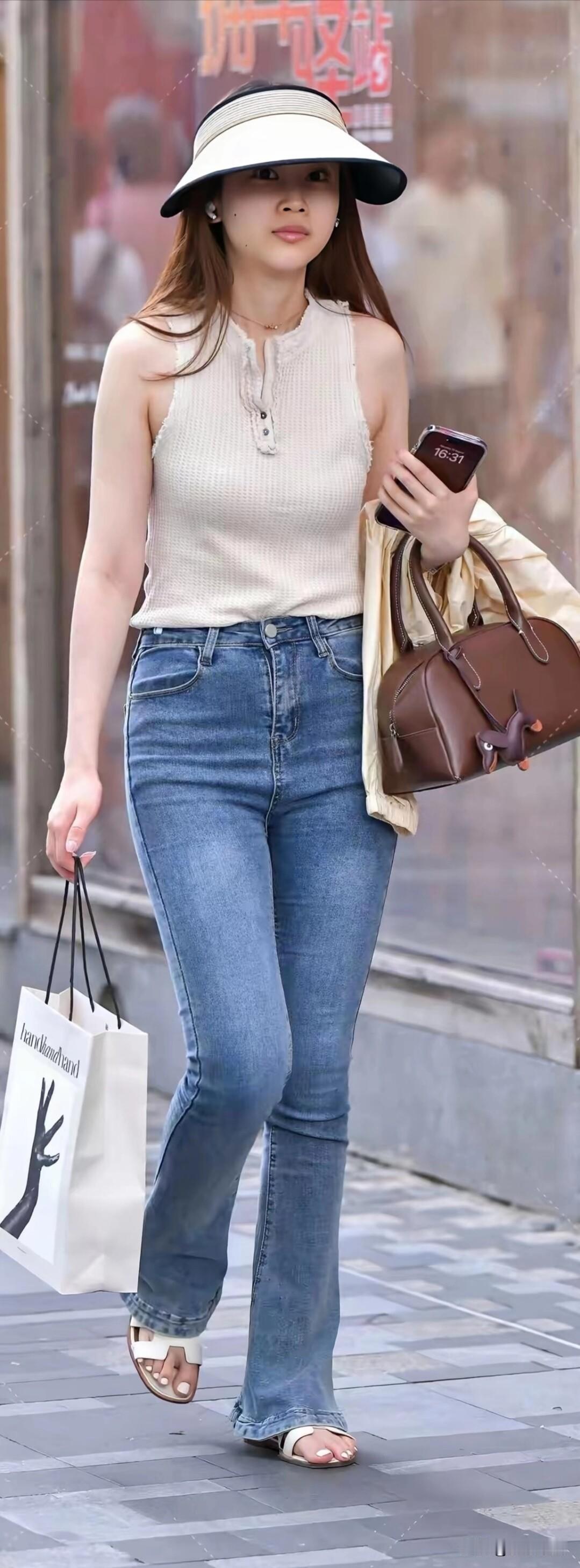 米白无袖针织衫搭配牛仔喇叭裤，遮阳帽和托特包增添休闲感，是夏日街头清爽又随性的穿