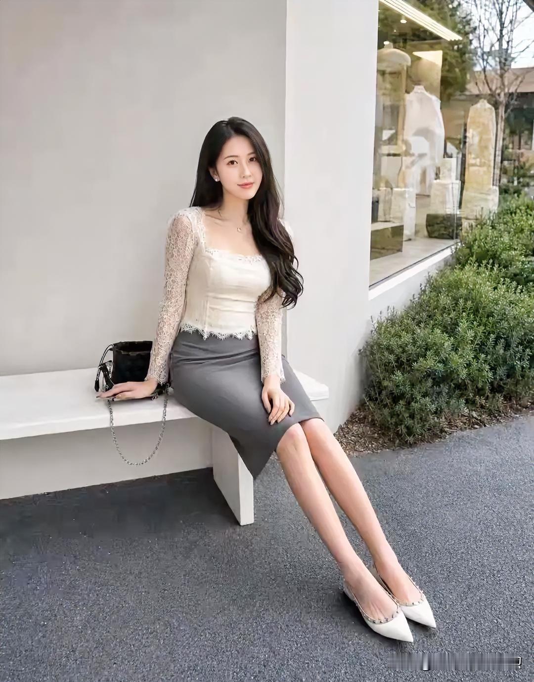 米白蕾丝轻绕柔肩，灰裙勾勒曼妙曲线。长发如瀑垂落，她静倚白凳，眸光温婉，将都市的