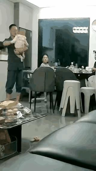 一男子抱着小婴儿站在饭桌旁，居然让孩子直接从自己的怀里倒翻下去，眼瞅着孩子在全家